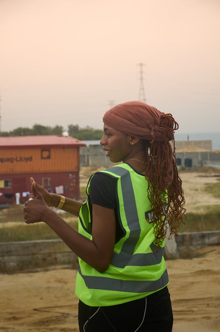 team-02 Confident female construction worker in safety vest giving thumbs up at a building site.